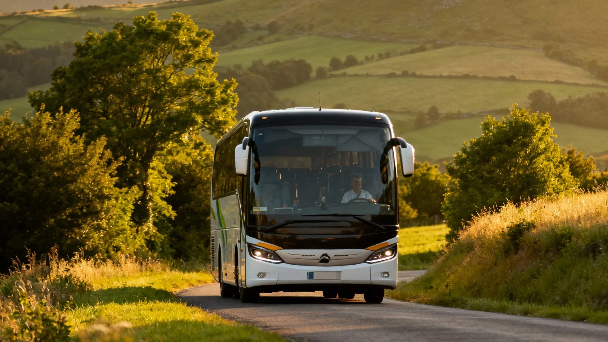 Autocar du réseau Cars Région Cantal roulant sur une route de campagne vallonnée, entourée de collines vertes et de prairies sous la lumière d’été.
