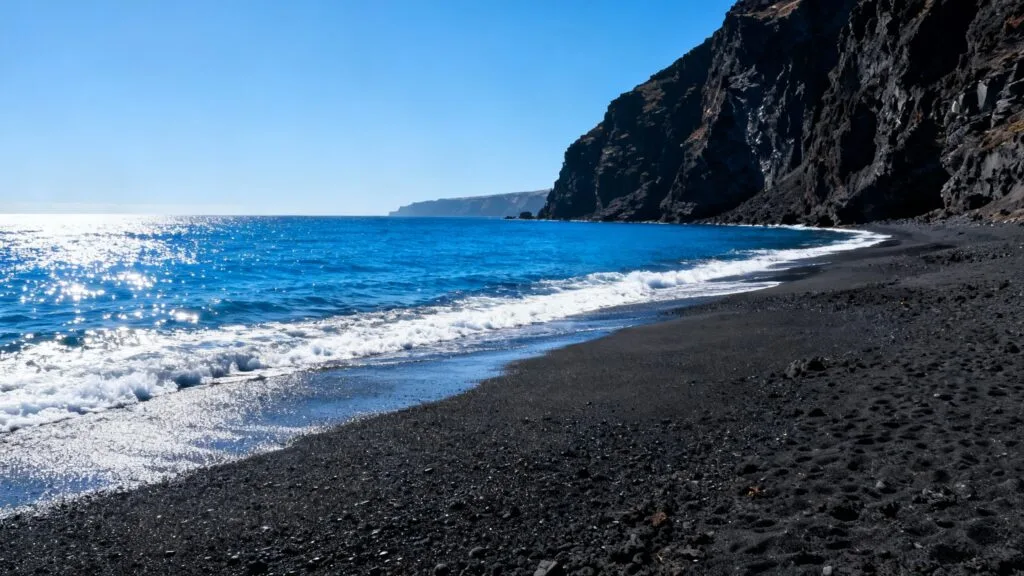 Plage de sable noir et falaises volcaniques ensoleillées