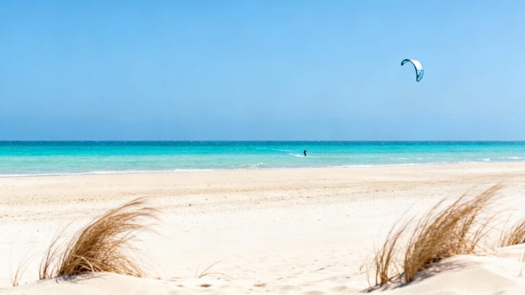 Grande plage dorée, eau turquoise, ciel clair et alizés