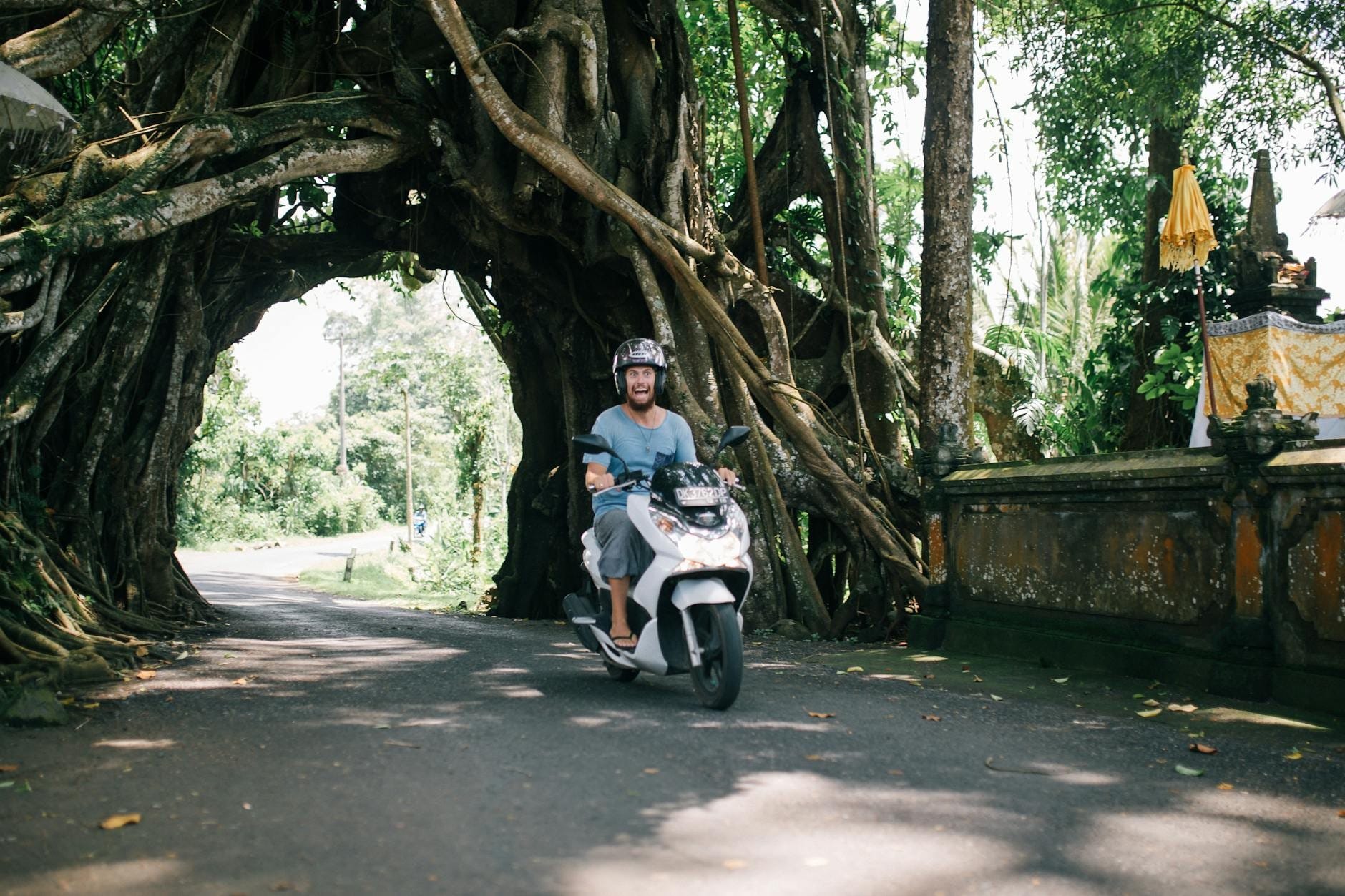 Touriste en scooter traversant une route ombragée à Bali