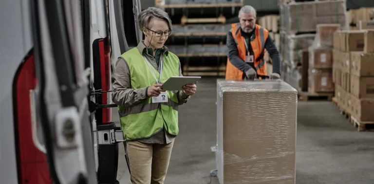 Femme logisticienne avec tablette devant une palette filmée dans un entrepôt B2B
